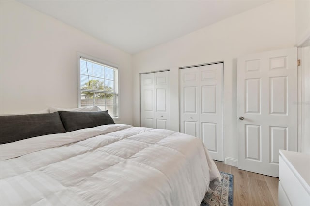 bedroom featuring light wood-type flooring, multiple closets, and vaulted ceiling