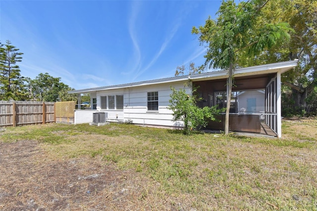 rear view of property with central air condition unit, fence, a lawn, and a sunroom