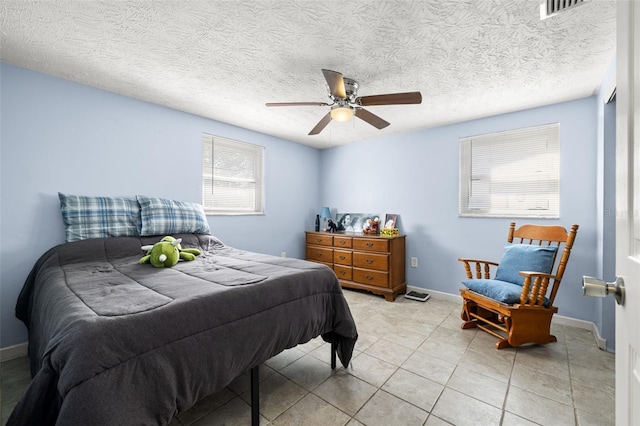 bedroom with visible vents, baseboards, light tile patterned floors, a textured ceiling, and a ceiling fan