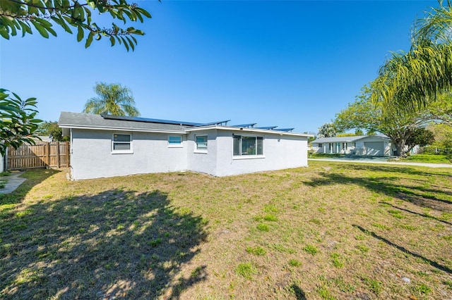 rear view of property with stucco siding, roof mounted solar panels, a yard, and fence