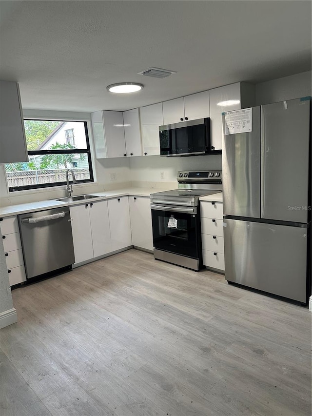 10216 N Pawnee Ave, Tampa, FL 33617 - kitchen with stainless steel appliances, light wood-type flooring, white cabinets, and light countertops