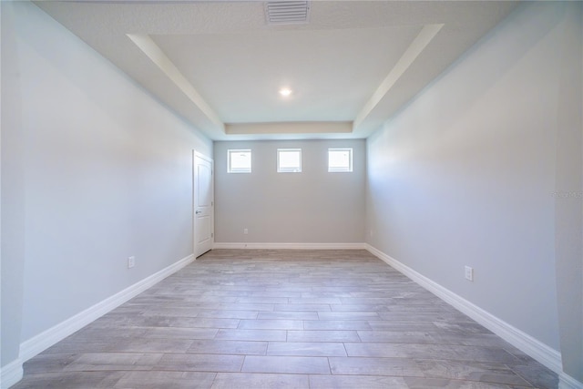 unfurnished room featuring visible vents, baseboards, light wood-style floors, and a tray ceiling