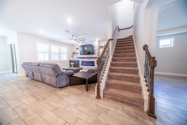 staircase featuring visible vents, baseboards, ceiling fan, a fireplace, and wood finished floors