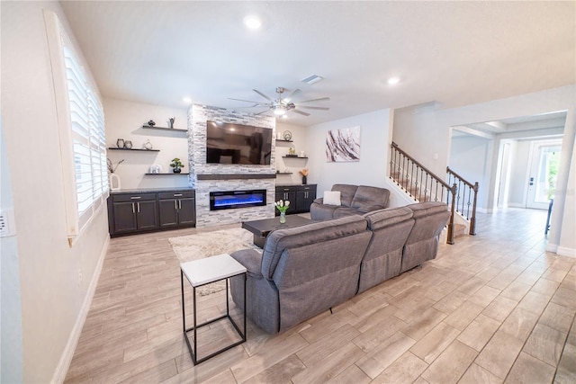 living area featuring visible vents, a large fireplace, light wood-style floors, ceiling fan, and stairs