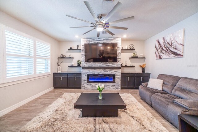 living area featuring a large fireplace, baseboards, light wood-style flooring, a textured ceiling, and a ceiling fan