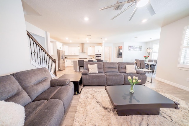 living room featuring a ceiling fan, baseboards, light wood finished floors, recessed lighting, and stairs