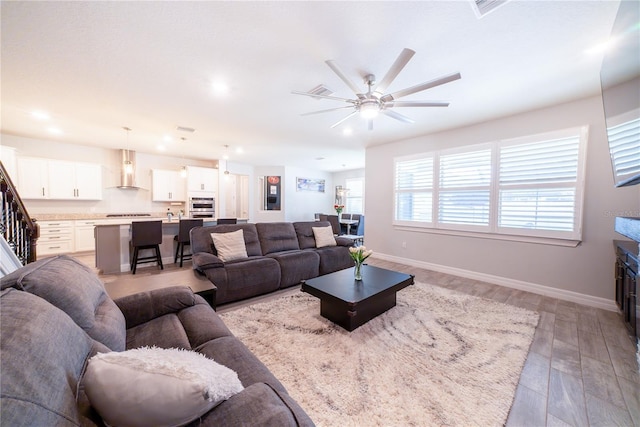living room with light wood-type flooring, baseboards, ceiling fan, and stairs