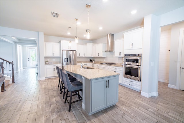 kitchen with visible vents, wood tiled floor, a breakfast bar, appliances with stainless steel finishes, and wall chimney exhaust hood