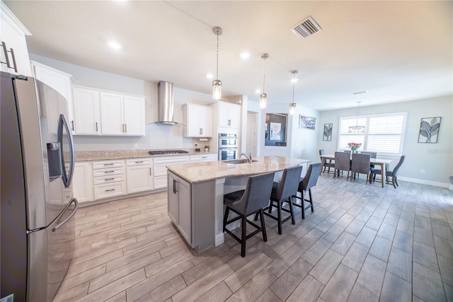 kitchen with visible vents, a center island with sink, appliances with stainless steel finishes, wall chimney exhaust hood, and wood tiled floor