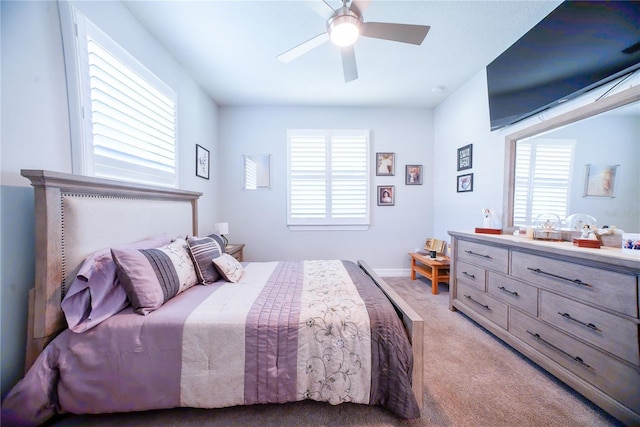 bedroom featuring baseboards, multiple windows, light colored carpet, and a ceiling fan