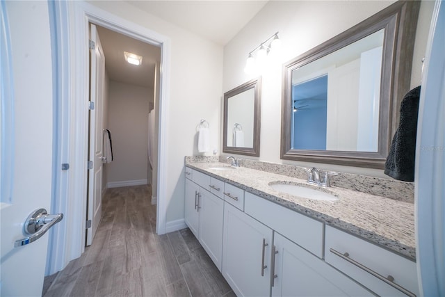 bathroom with double vanity, wood finished floors, baseboards, and a sink