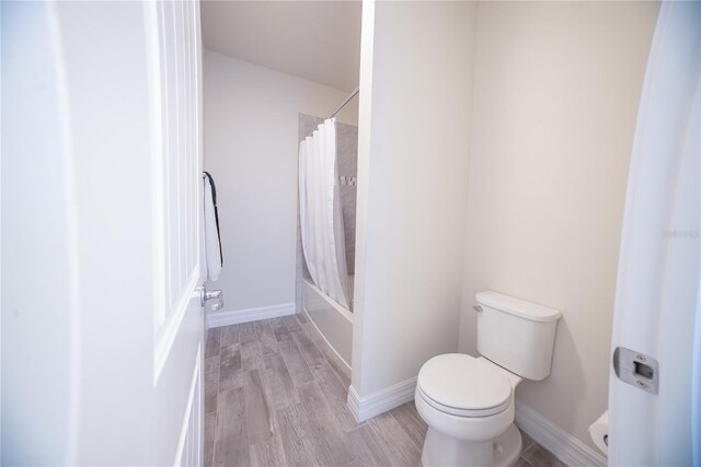 bathroom with shower / bath combination with curtain, toilet, baseboards, and wood finished floors
