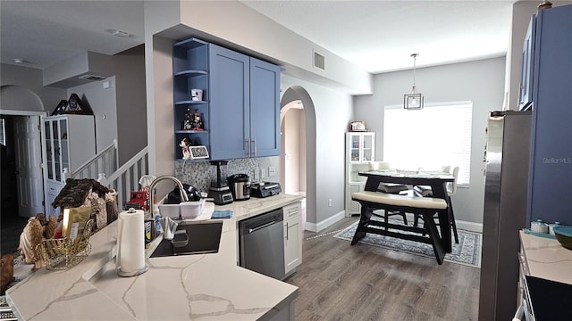 kitchen featuring light stone counters, wood finished floors, a sink, stainless steel appliances, and backsplash