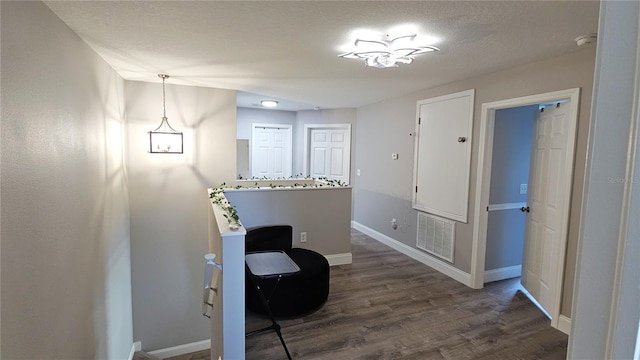 corridor featuring dark wood-style floors, visible vents, a textured ceiling, and baseboards