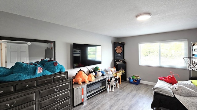 bedroom with baseboards, a textured ceiling, and light wood-style flooring