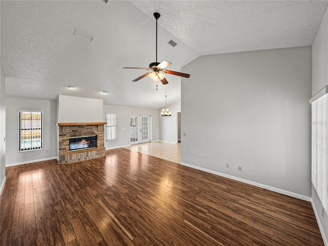 unfurnished living room featuring wood finished floors, visible vents, baseboards, a fireplace, and ceiling fan with notable chandelier