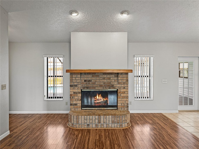 unfurnished living room with a brick fireplace, wood finished floors, and baseboards