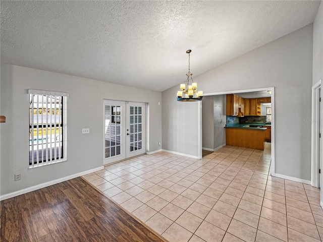 unfurnished dining area with lofted ceiling, a notable chandelier, french doors, and baseboards