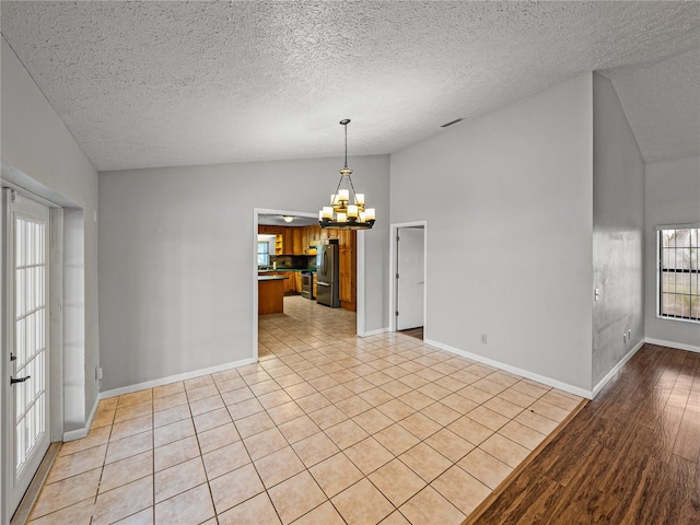 spare room featuring visible vents, a notable chandelier, light wood-style floors, baseboards, and vaulted ceiling