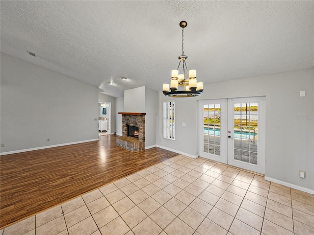 unfurnished living room featuring visible vents, light tile patterned flooring, french doors, a brick fireplace, and a chandelier