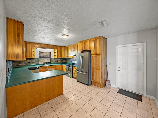 kitchen with visible vents, appliances with stainless steel finishes, a peninsula, brown cabinetry, and decorative backsplash