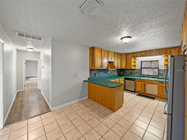 kitchen featuring visible vents, stainless steel appliances, a peninsula, light tile patterned floors, and decorative backsplash