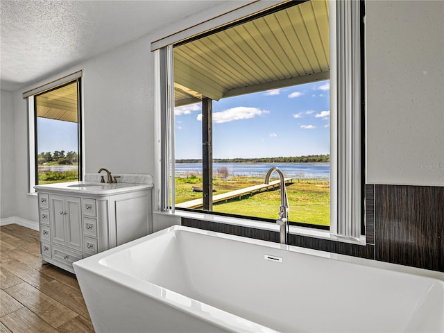 bathroom featuring vanity, wood finished floors, a freestanding tub, a water view, and a textured ceiling