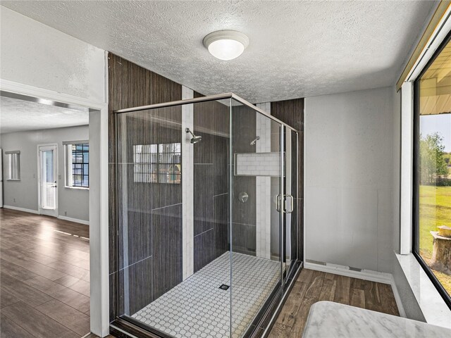 full bath with baseboards, a textured ceiling, wood finished floors, and a shower stall