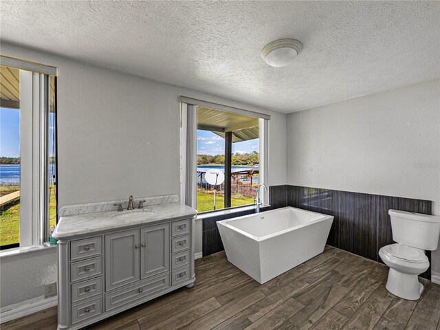 bathroom with toilet, a textured ceiling, wood finished floors, a freestanding bath, and vanity