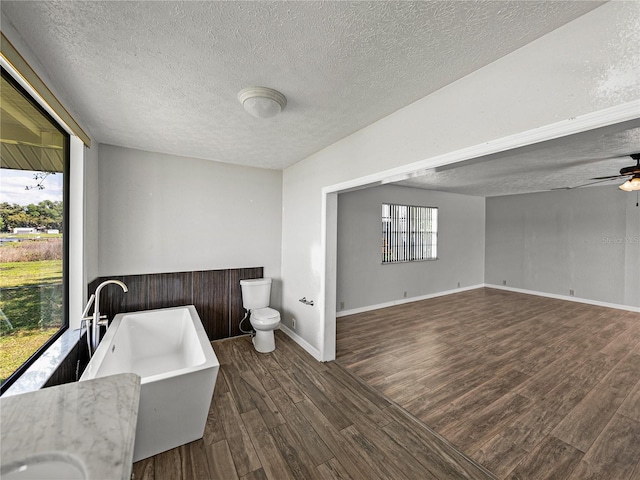 full bath featuring toilet, a freestanding bath, wood finished floors, a textured ceiling, and a ceiling fan