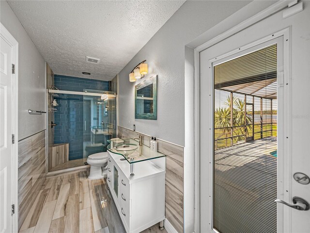 full bath featuring visible vents, a textured ceiling, wood finished floors, a shower stall, and vanity
