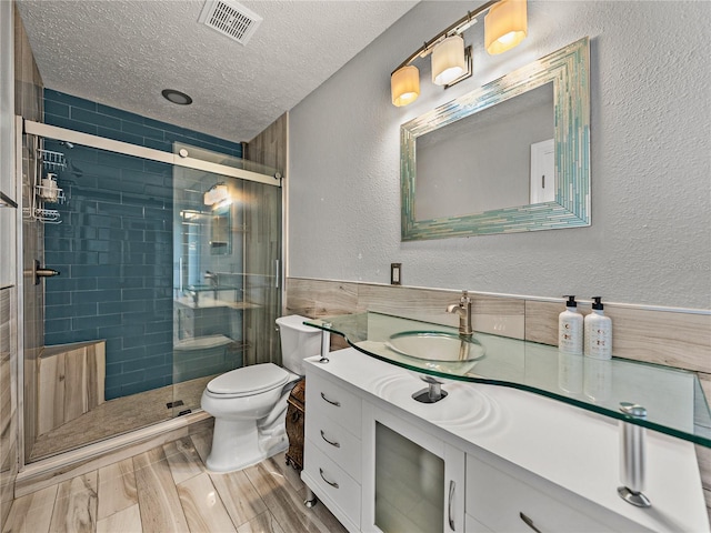 bathroom featuring visible vents, toilet, a stall shower, a textured ceiling, and a textured wall