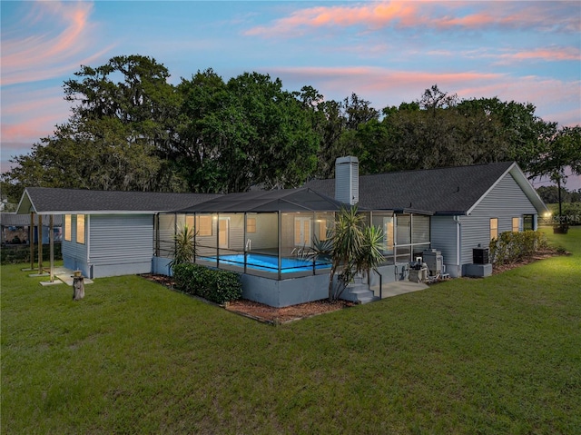 back of property at dusk featuring a lanai, an outdoor pool, central AC, and a yard