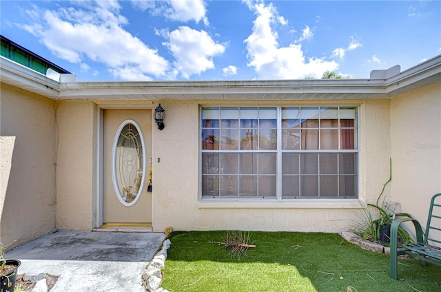 entrance to property with a yard and stucco siding