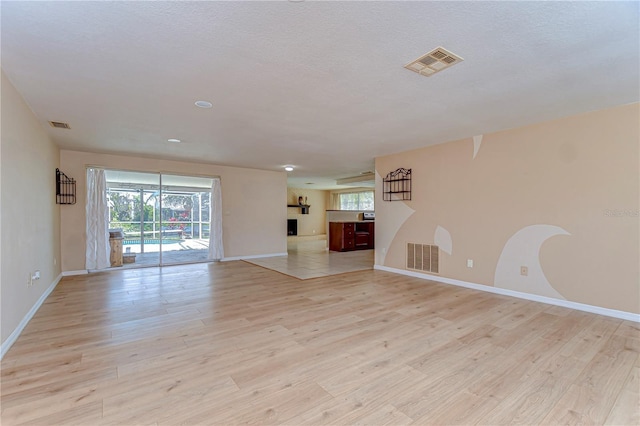 unfurnished living room featuring visible vents, plenty of natural light, and light wood finished floors