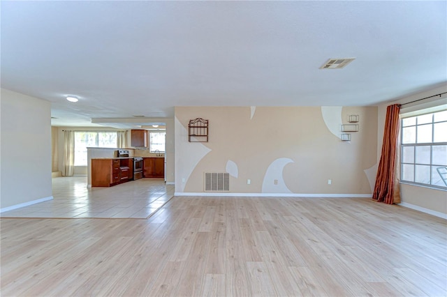 unfurnished living room with light wood-style floors, visible vents, and a wealth of natural light