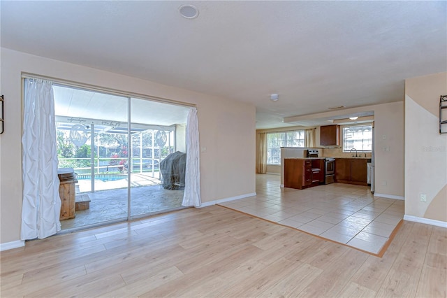 kitchen with a sink, baseboards, light wood finished floors, and stainless steel range with electric cooktop