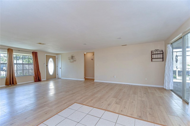 unfurnished living room featuring light wood-style flooring, baseboards, and a healthy amount of sunlight