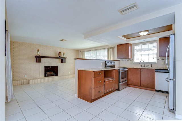 kitchen with visible vents, brick wall, stainless steel appliances, open floor plan, and brown cabinets