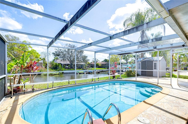 outdoor pool featuring glass enclosure, an outbuilding, a storage unit, a water view, and a patio area