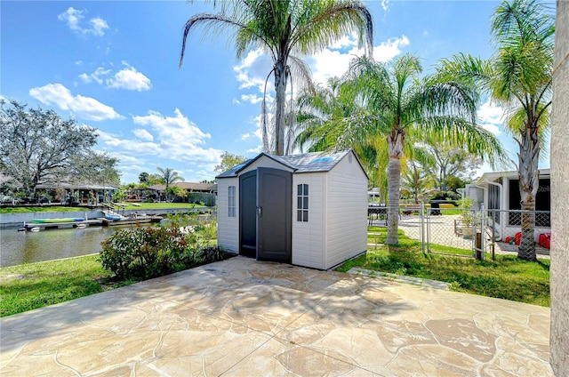 view of patio / terrace featuring a storage shed, fence, a water view, and an outbuilding