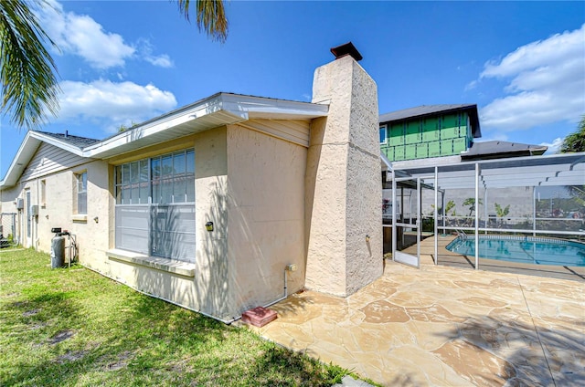 back of property with glass enclosure, a patio, an outdoor pool, a chimney, and a lawn