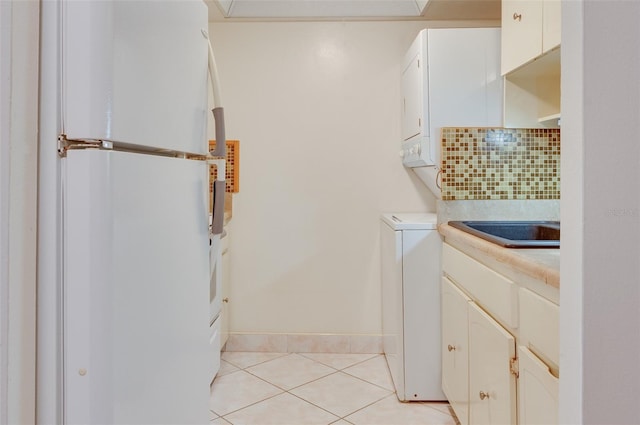 laundry room featuring light tile patterned floors, baseboards, and stacked washer / drying machine