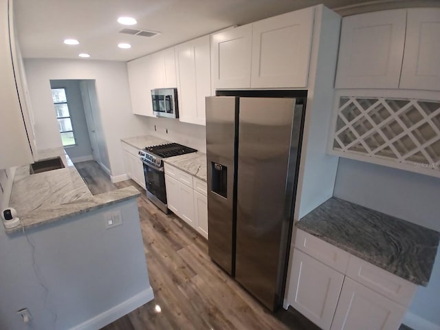 kitchen with light stone countertops, white cabinetry, wood finished floors, and stainless steel appliances