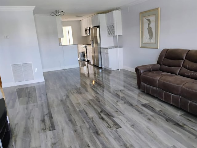 living room featuring wood finished floors, baseboards, ornamental molding, and visible vents