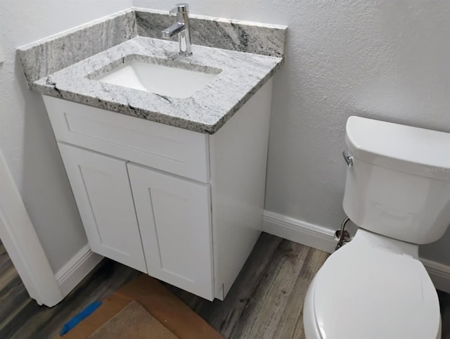half bath featuring toilet, baseboards, vanity, and wood finished floors