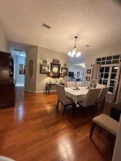 dining area featuring visible vents, wood finished floors, a textured ceiling, and a chandelier