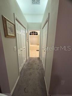 hall with baseboards, visible vents, and dark carpet