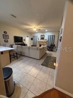 living area with light tile patterned flooring, a fireplace, baseboards, and a ceiling fan