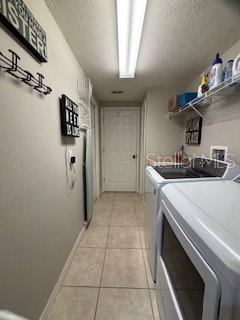 washroom with light tile patterned floors, baseboards, laundry area, a textured ceiling, and washer and clothes dryer